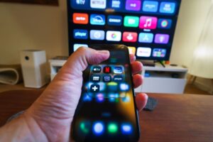 Mão segurando smartphone apontado para uma TV em sala de estar exibindo a interface com os melhores aplicativos para Android TV.