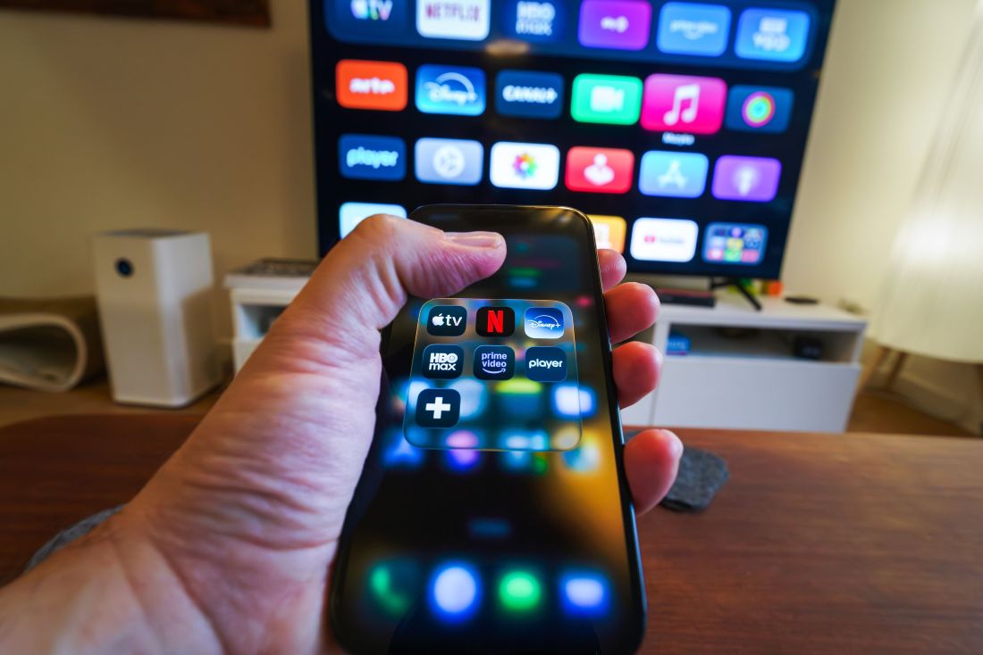 Mão segurando smartphone apontado para uma TV em sala de estar exibindo a interface com os melhores aplicativos para Android TV.